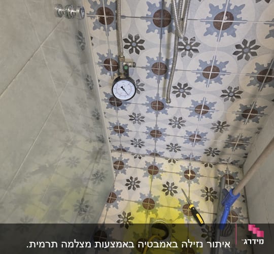 מד לחץ מים על רצפת מקלחת עם אריחים צבעוניים